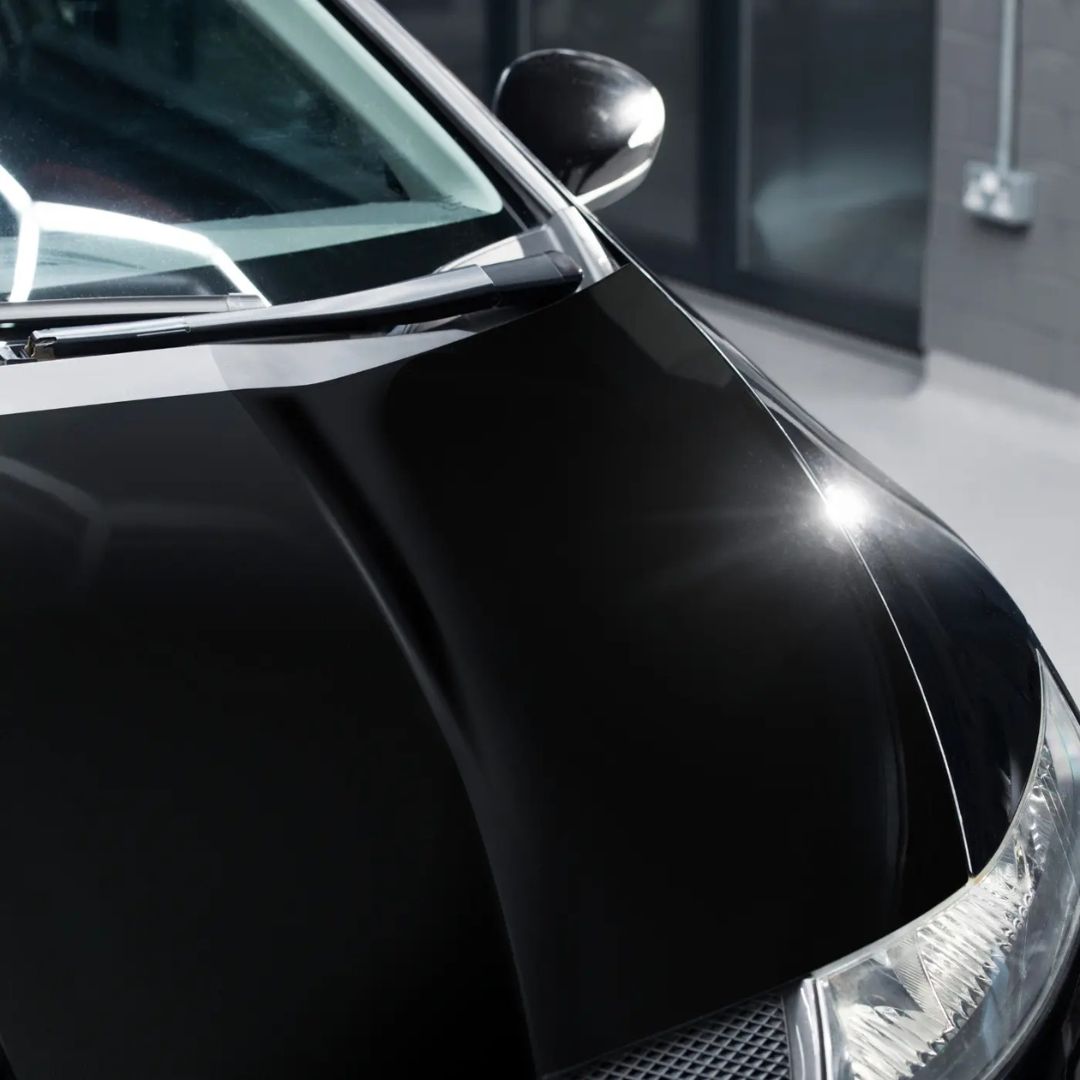 Close-up of a black car's side mirror and headlight in a garage.