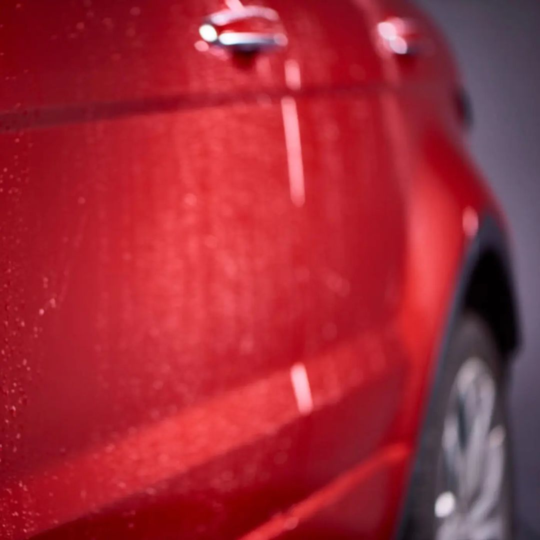 Close-up of a red car's side with water droplets on a dark background