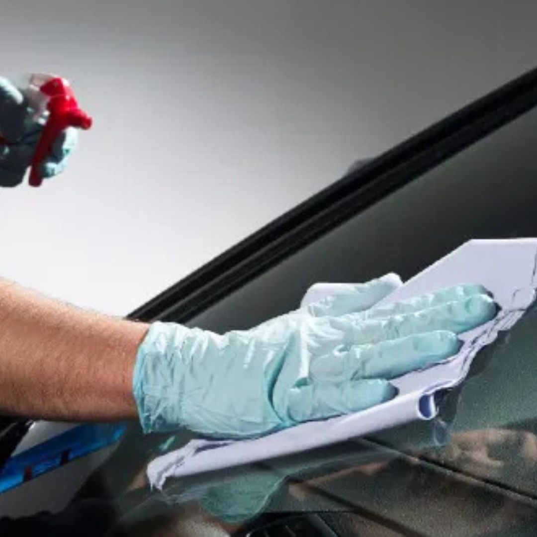 Person cleaning a car window with a cloth and spray bottle, wearing gloves.