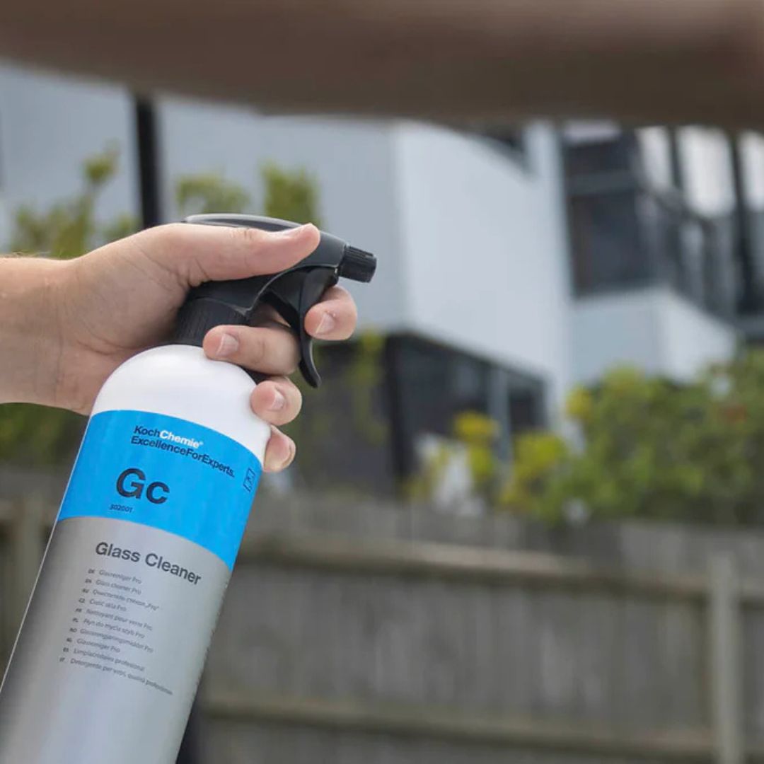 Hand holding a bottle of Koch Chemie GC glass cleaner with a blurred outdoor background