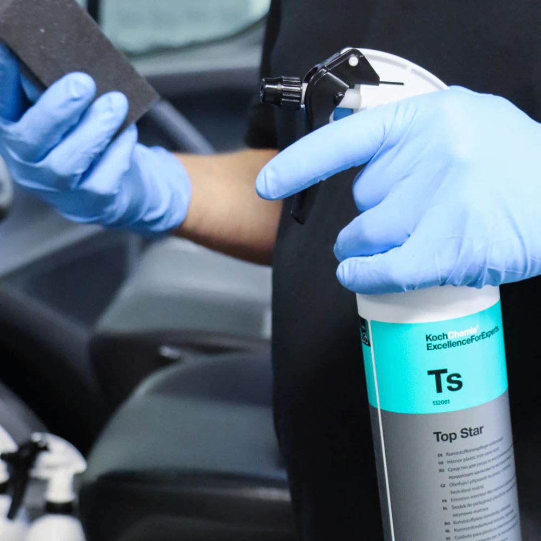 Person wearing blue gloves holding a can of Koch Top Star spray and a sanding block inside a car.