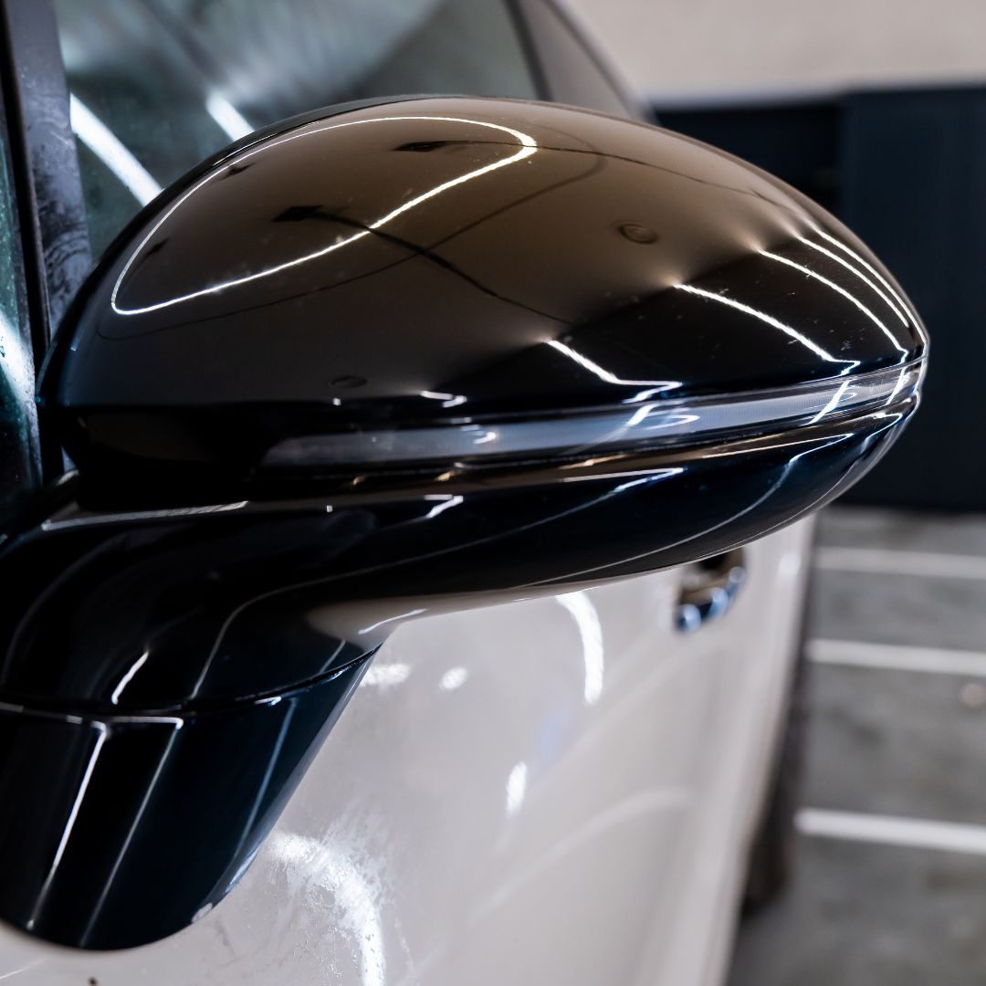 Close-up of a car's black PPF side mirror on a white car.