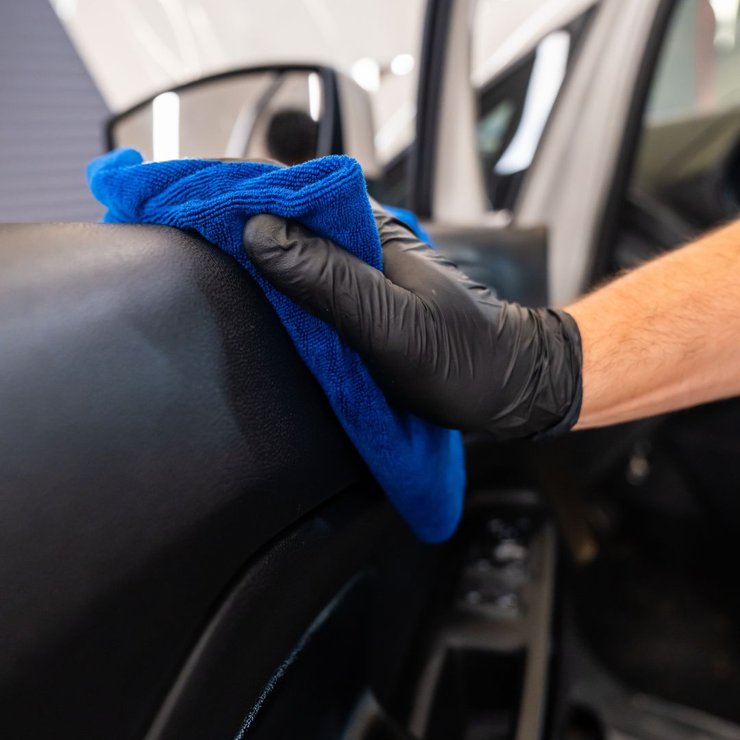 Person cleaning a car interior with a blue microfiber cloth and black gloves.