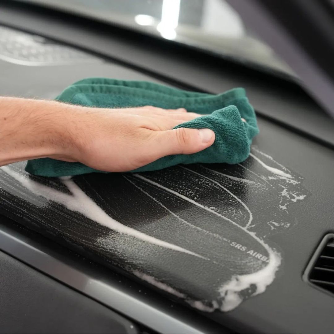 Maniac Multisurface Cleaner being wiped off a car dashboard with a green cloth.