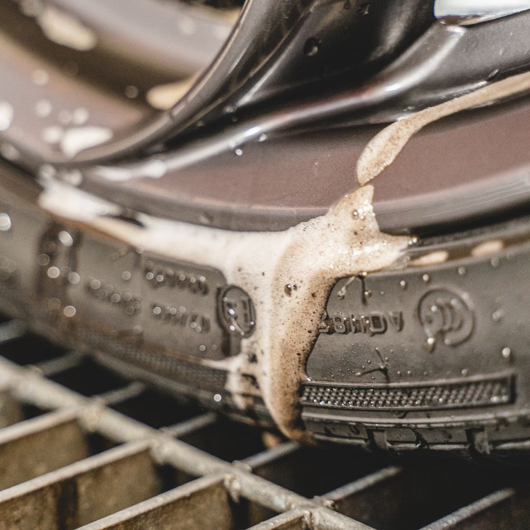 Close-up of a tyre cleaner with soap suds on a wheel and tyre surface.