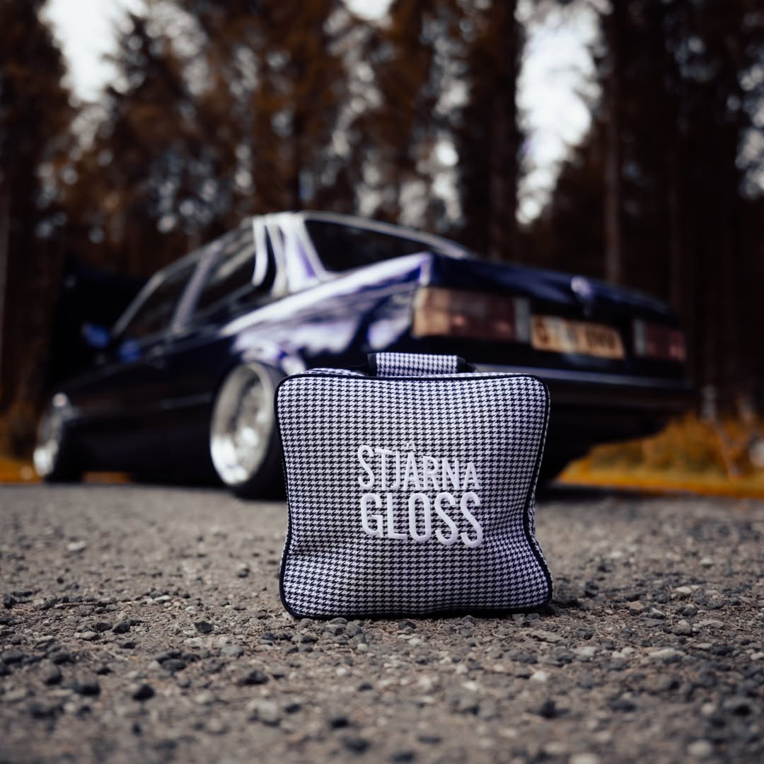 Black and white checkered pouch with 'Starna Gloss' text on a road with a blurred car in the background.