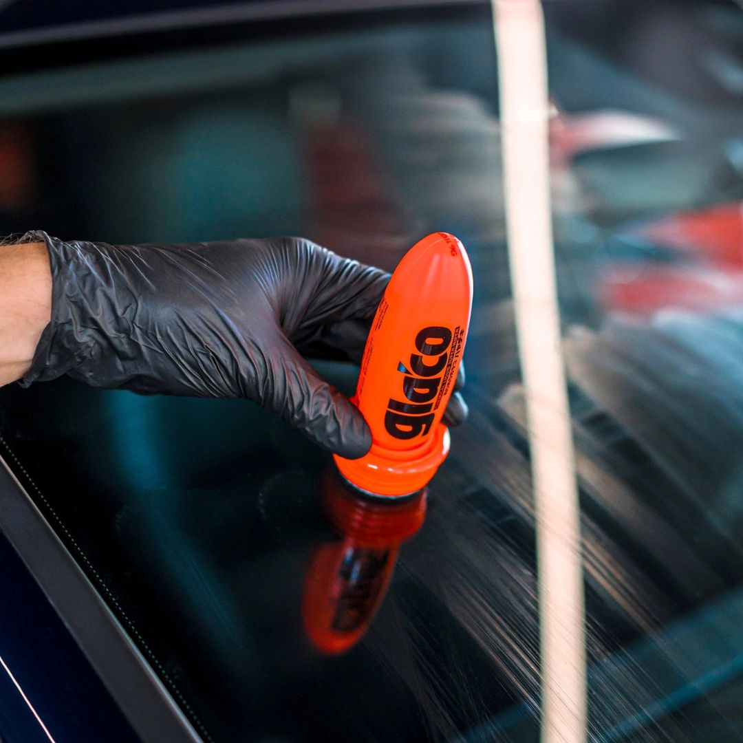 Person cleaning a car window with an orange Glaco product.