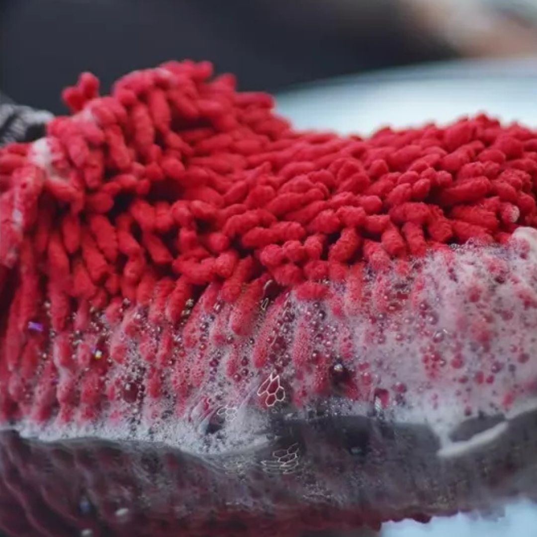 Red microfibre wash mitt with soap suds on a car surface