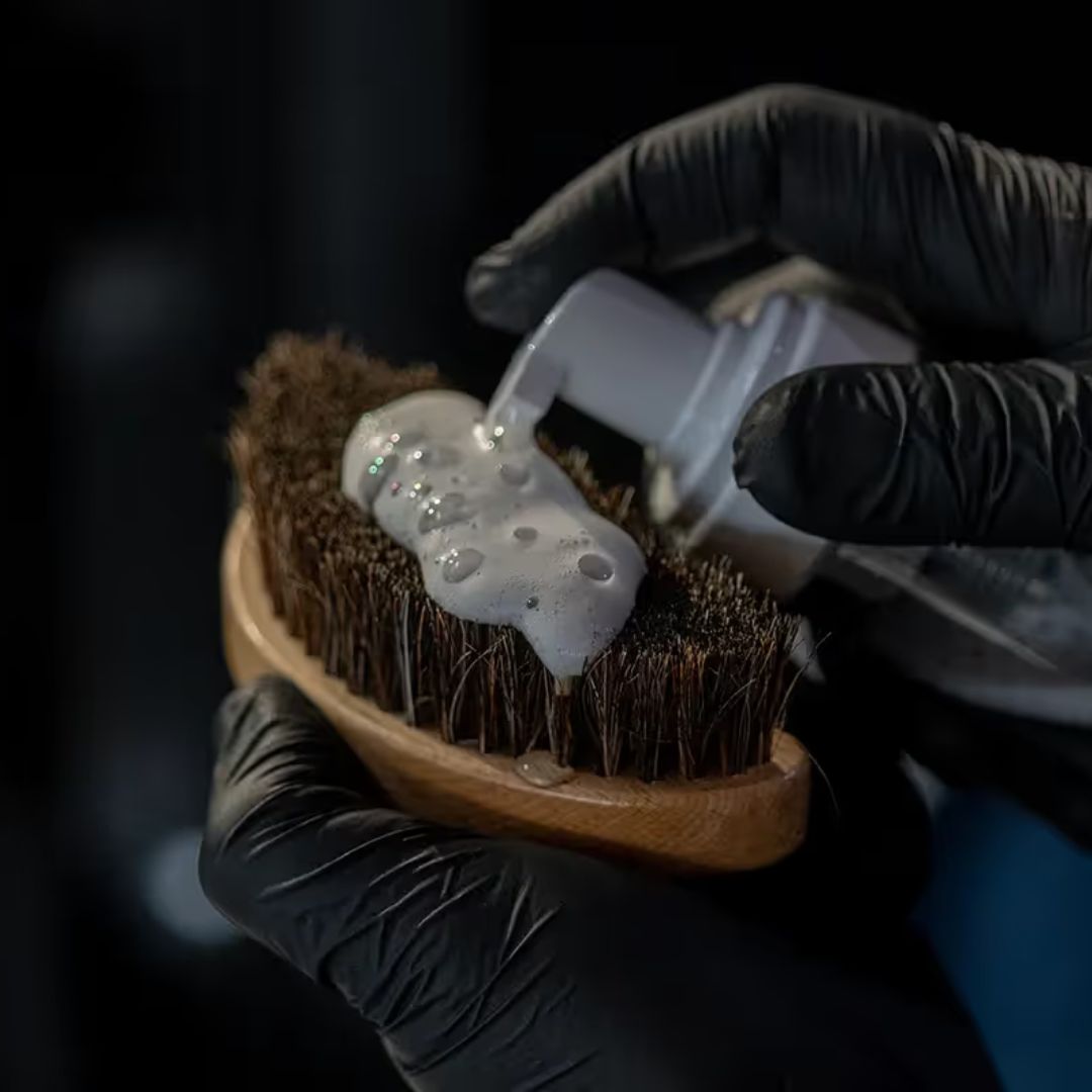 Person applying soap to a brush with black gloves on a dark background