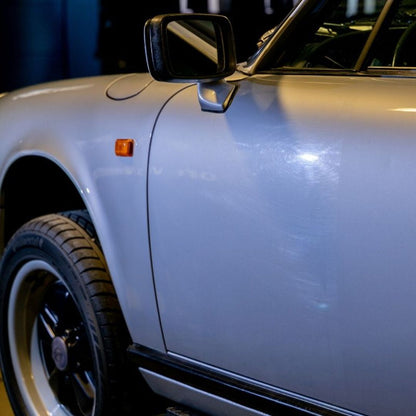 Close-up of a light blue 911 SC side door, mirror and wheel with before and after polishing