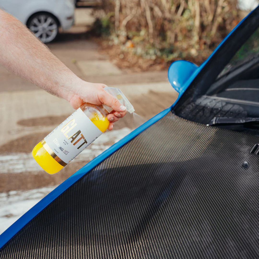 Person applying a Stjarnagloss Glatt Rinseaid to a car's carbon fibre bonnet with a blurred outdoor background