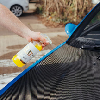 Person applying a Stjarnagloss Glatt Rinseaid to a car's carbon fibre bonnet with a blurred outdoor background