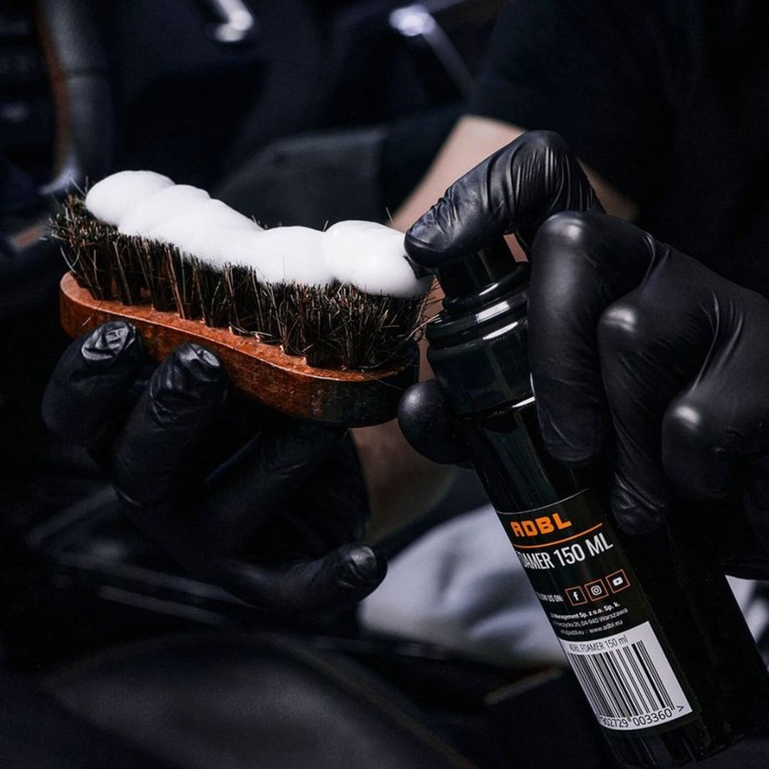 Person holding a brush with foam and a bottle labeled 'ADBL' in a dark setting