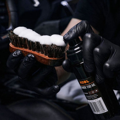 Person holding a brush with foam and a bottle labeled 'ADBL' in a dark setting
