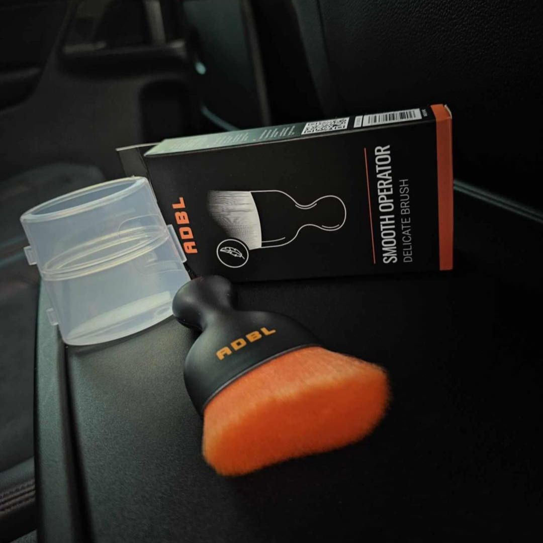 ADBL Smooth Operator Ultra Soft Interior Brush ADBL car detailing brush with packaging and container on a car seat.