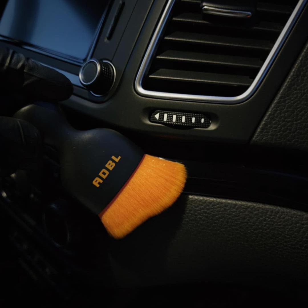 ADBL Smooth Operator Ultra Soft Interior Brush Car interior cleaning brush with orange bristle head and black handle inside a vehicle.