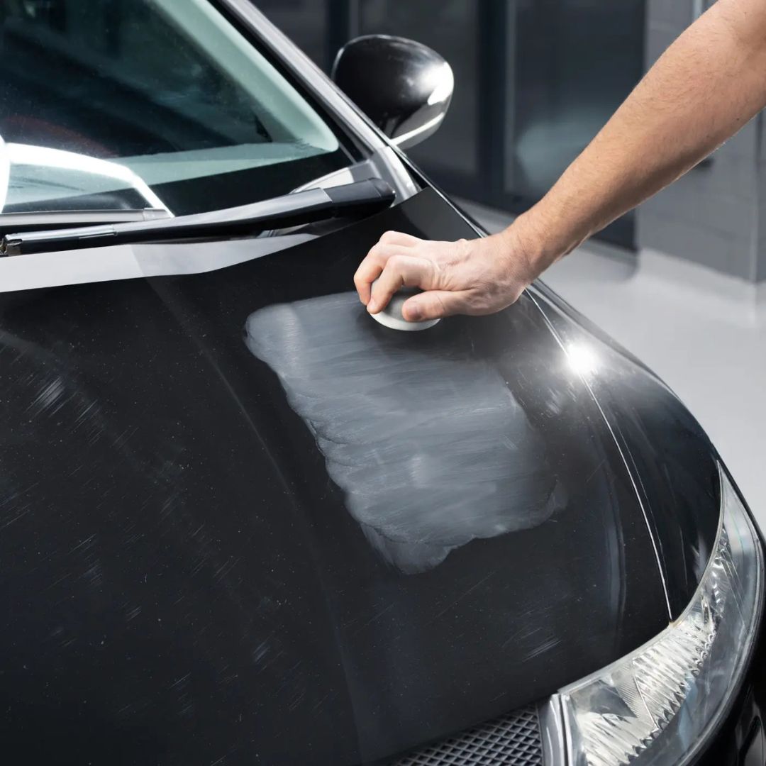 Person applying Autoglym Advanced Paint Restorer polish to a black car by hand