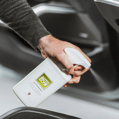Person holding an Autoglym Autofresh spray bottle with a green label inside a car.