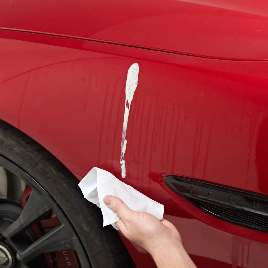 Person cleaning a red car with a white cloth