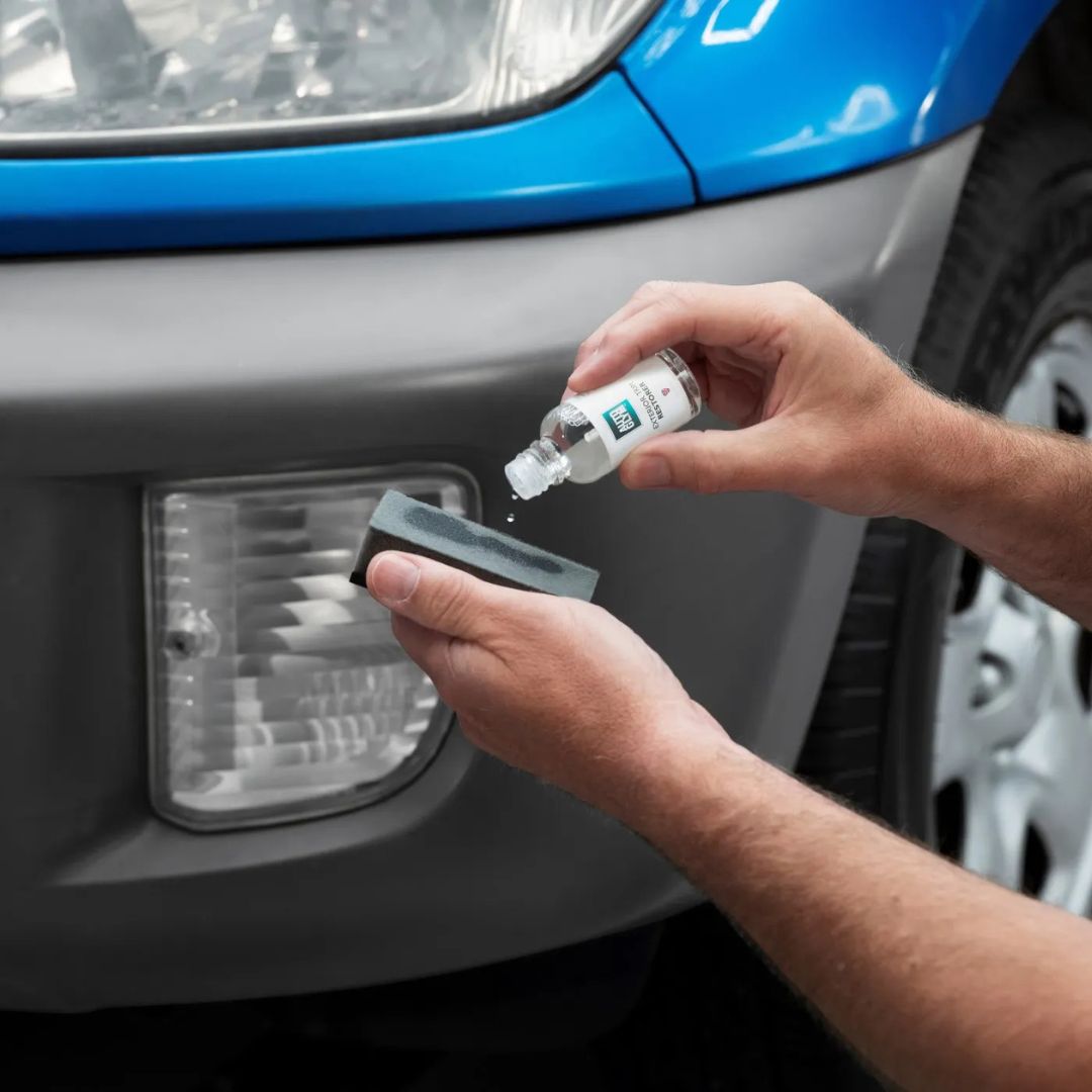 Person applying a clear liquid to a car's headlight using a small bottle and applicator.