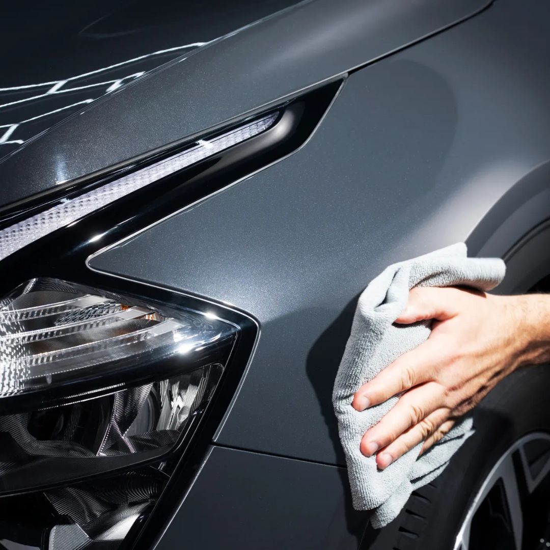 Person cleaning a car's headlight with Autoglym finishing cloths in grey