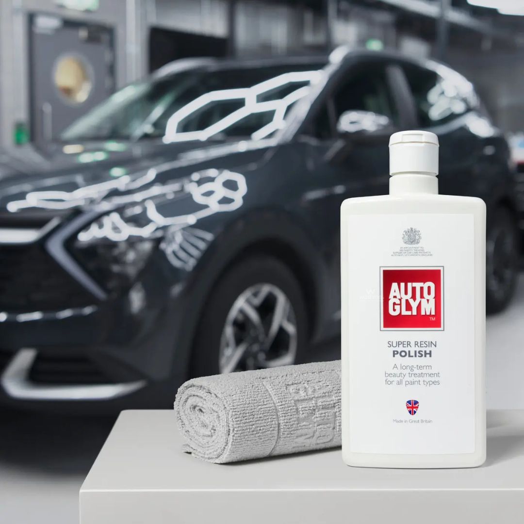 Autoglym Super Resin Polish bottle with Autoglym finishing cloths in front of a car in a garage.