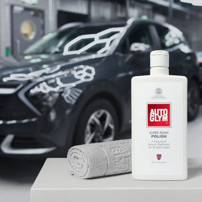 Autoglym Super Resin Polish bottle with Autoglym finishing cloths in front of a car in a garage.