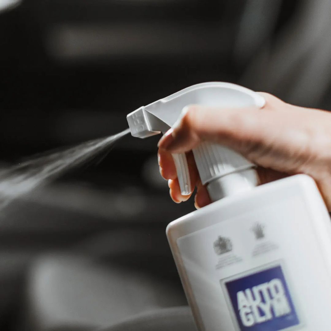 Hand holding a spray bottle labeled 'Autoglym' with a dark background