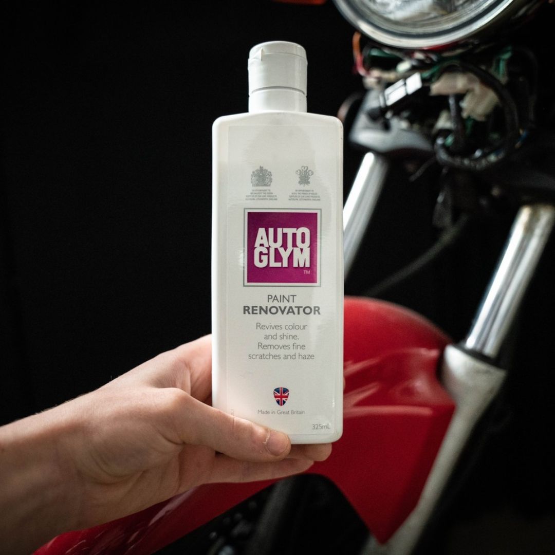 Hand holding a bottle of Autoglym Paint Renovator in front of a motorcycle.