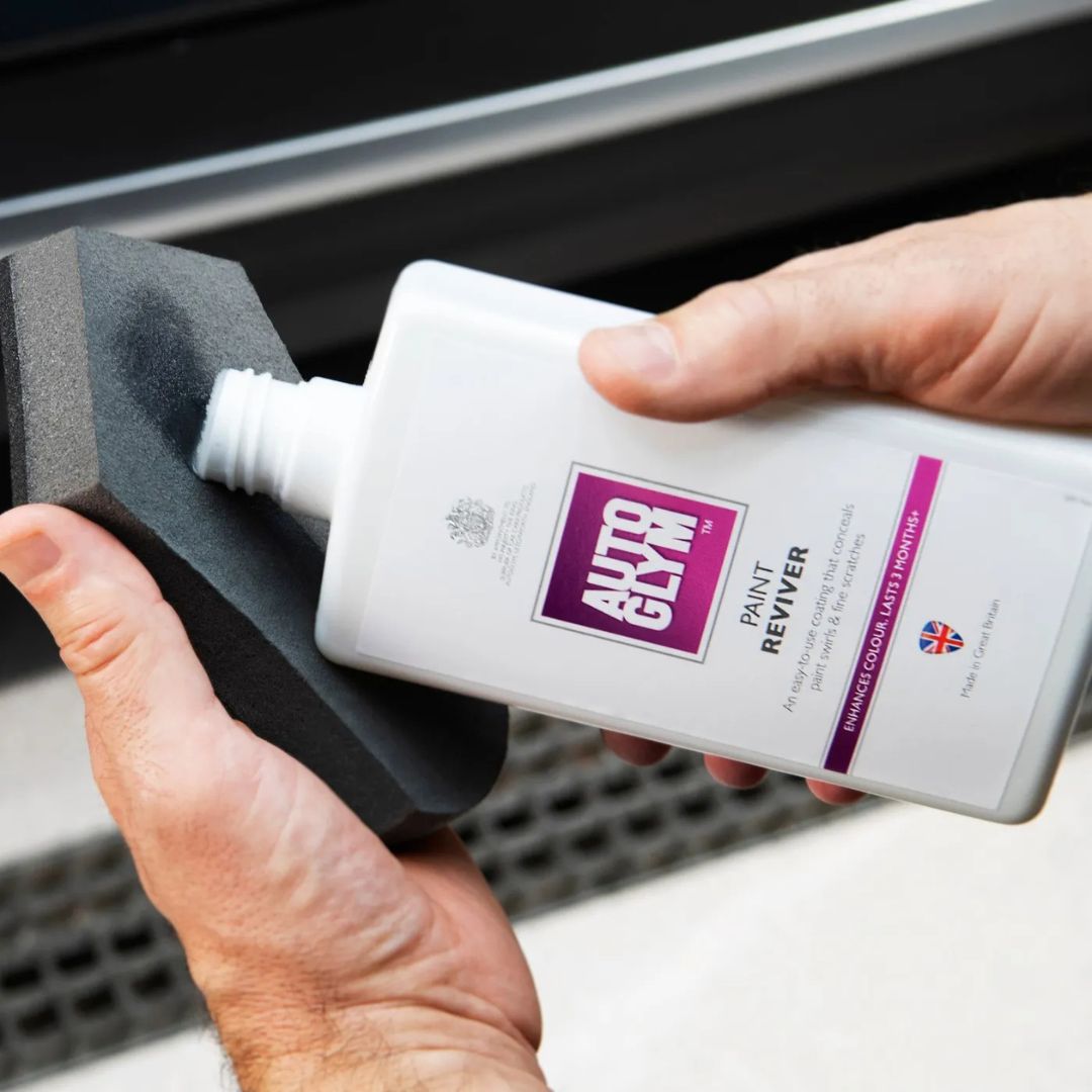 Person holding a bottle of Autoglym Paint Reviver with a black foam applicator.