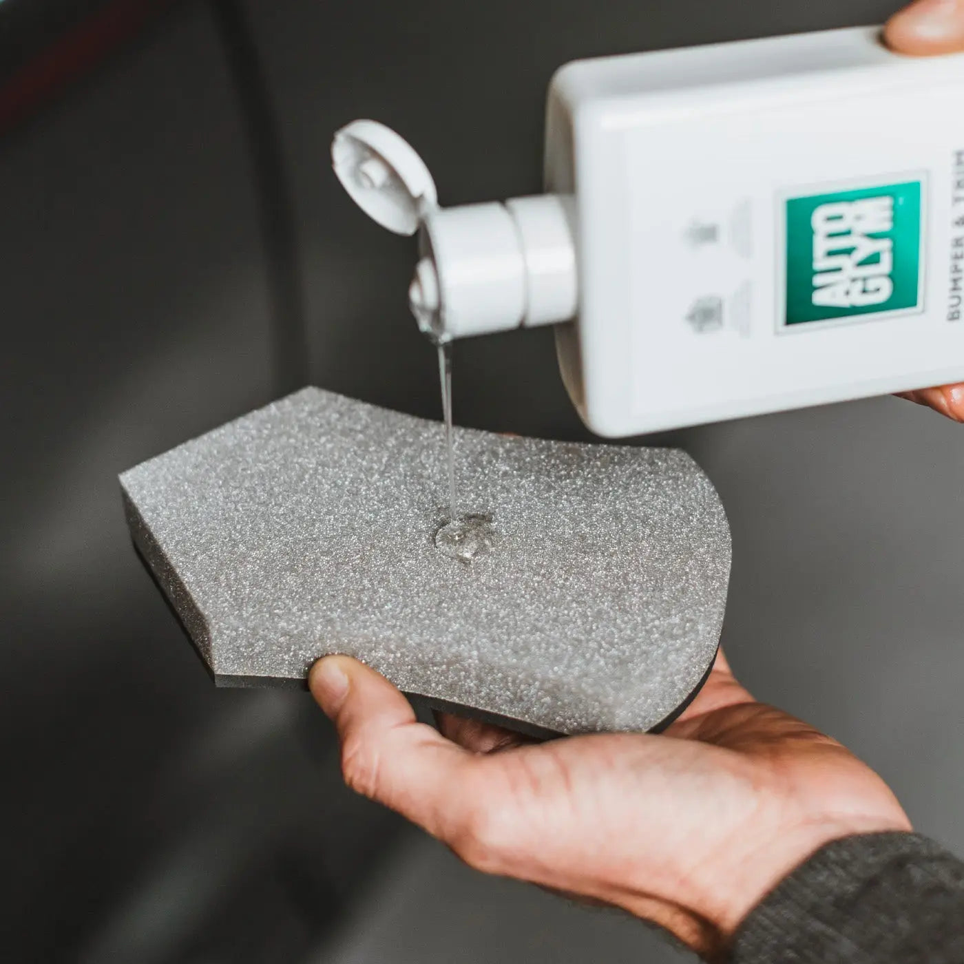 Person applying a white cream from a bottle labeled 'Autoglym' onto a grey sponge.