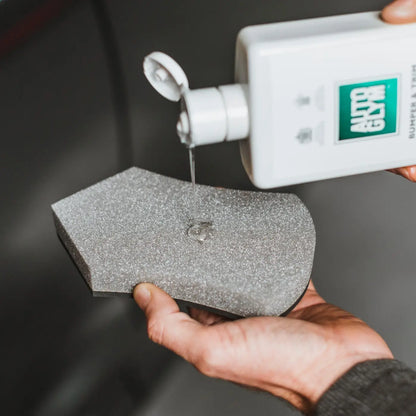 Person applying a white cream from a bottle labeled 'Autoglym' onto a grey sponge.