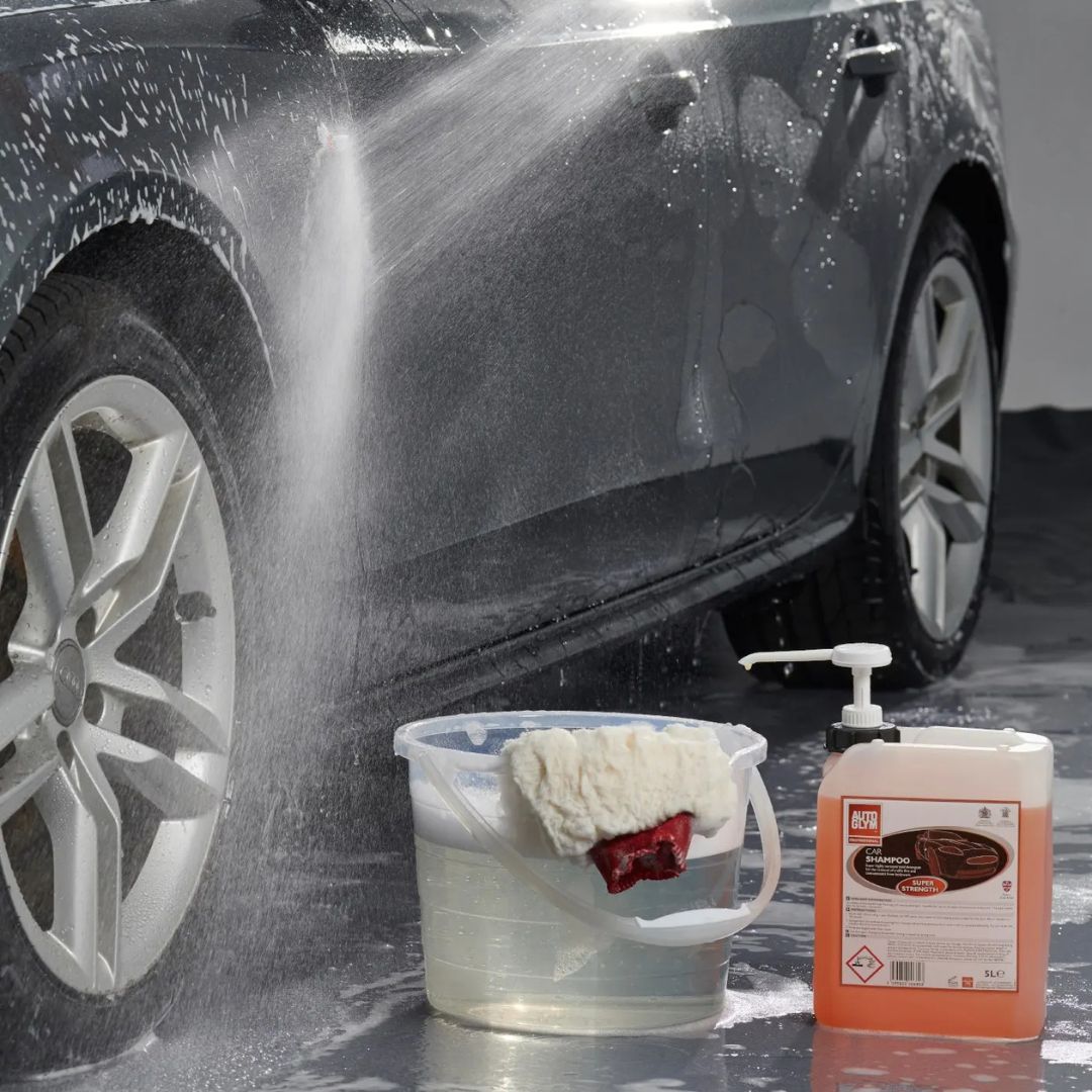 Car being washed with a bucket of soapy water and a bottle of car wash soap.