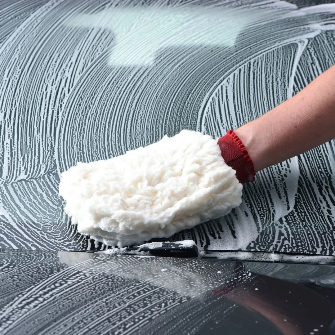 Person cleaning a car window with a white foam mitt and red handle.