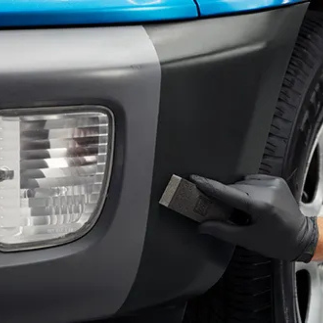 Person wearing a black glove applying a black strip to a vehicle's headlight area.