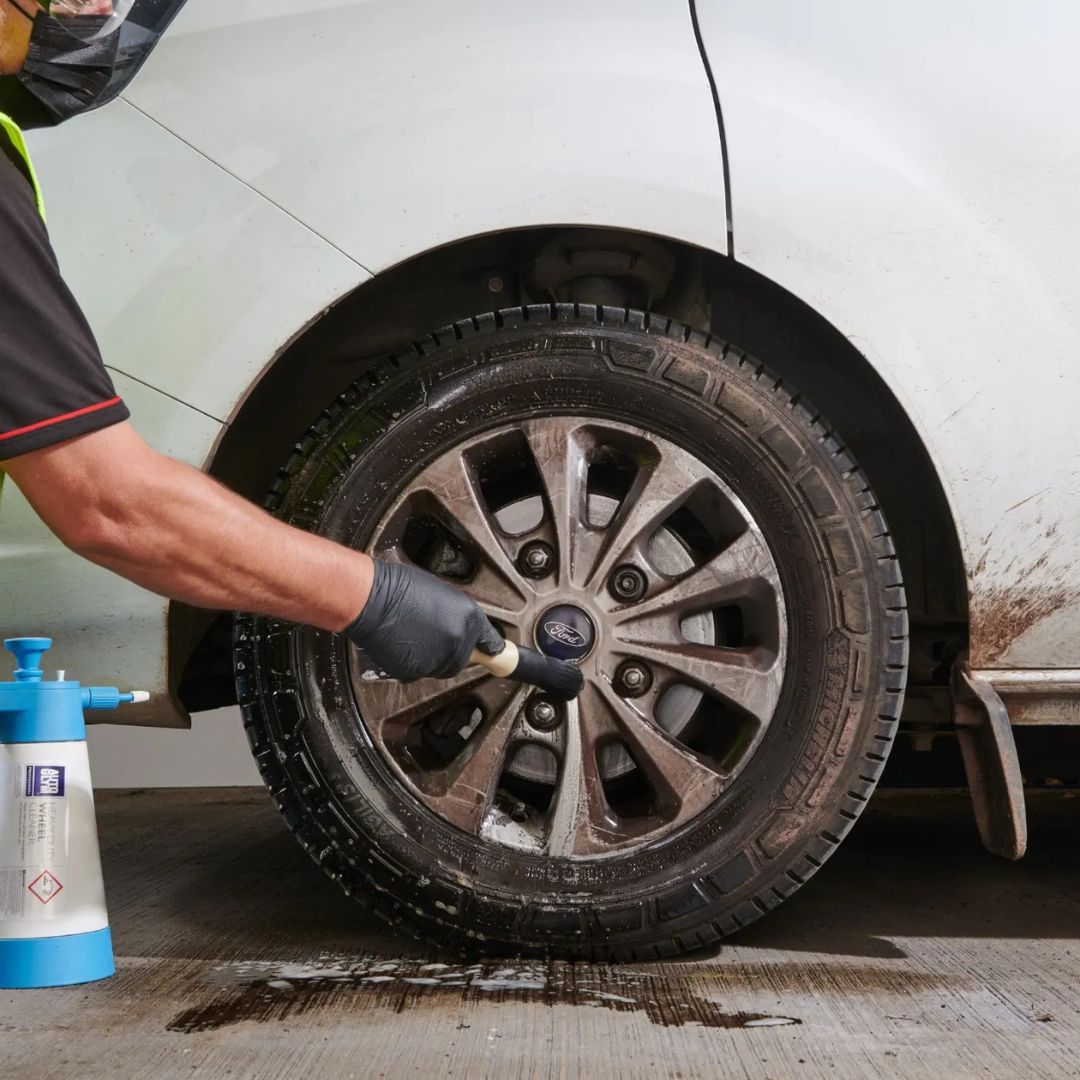 Person cleaning a wheel and tire on a Ford with a brush with Autoglym Heavy Duty Wheel Cleaner 