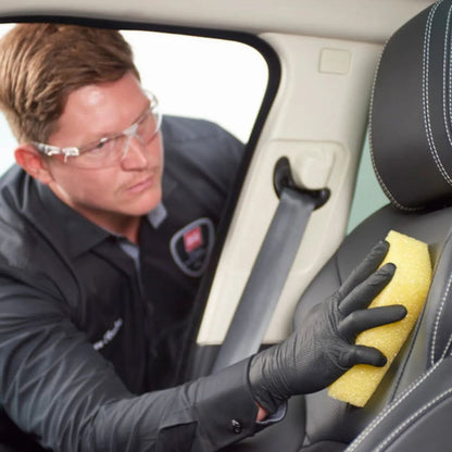 Person cleaning car interior with a yellow sponge and protective glasses