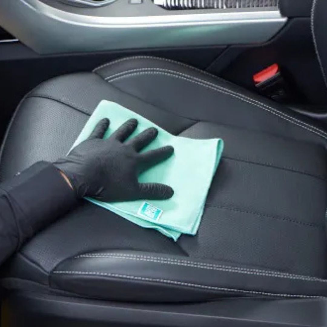 Person cleaning a car seat with a green cloth and black glove