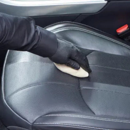 Person cleaning a car seat with a sponge and black gloves