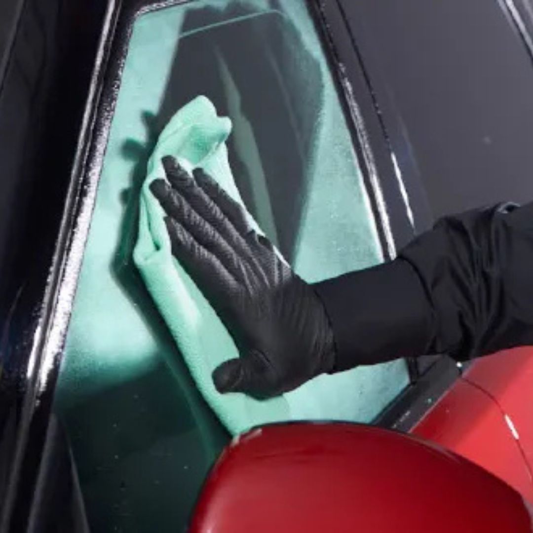 Person cleaning a car window with a green cloth and black gloves