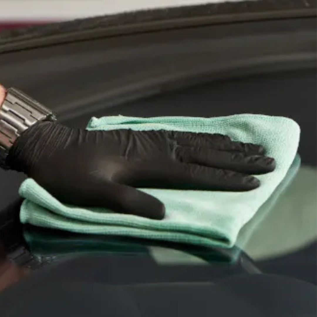Hand wearing a black glove holding a green microfiber cloth on a car surface