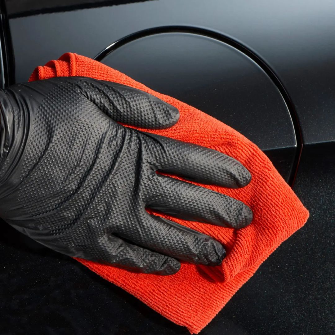Hand wearing a black glove holding an red Autoglym microfibre cloth against a car door handle.