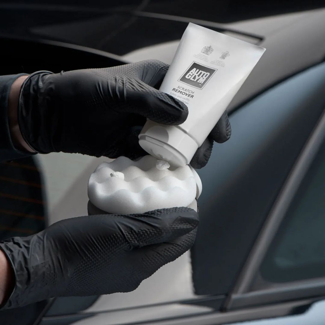 Person holding a tube of car polish with a car in the background