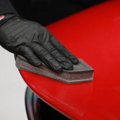 Person wearing black gloves using a sanding block on a red surface