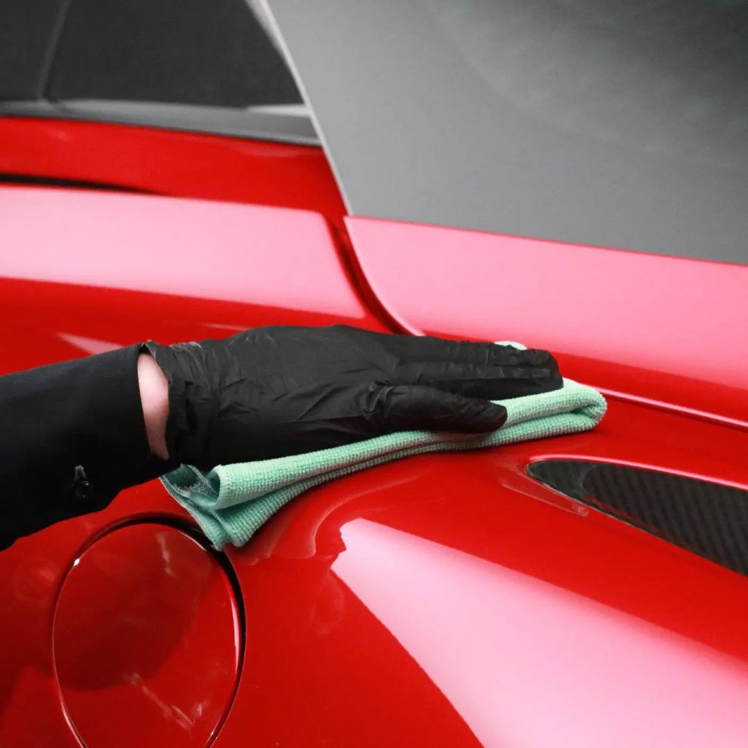 Person cleaning a red car with a green cloth and black gloves