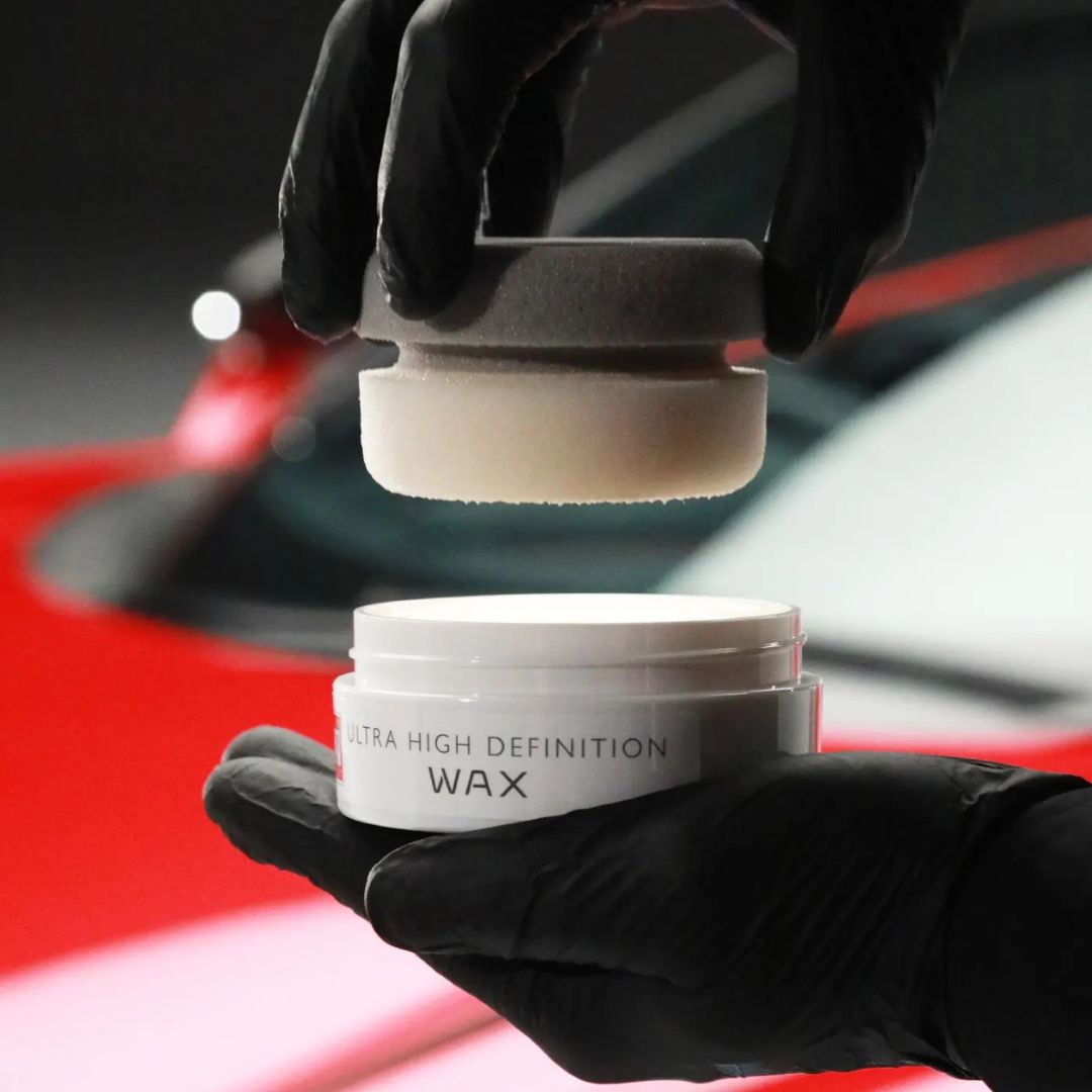 Person holding Ultra High Definition Wax with a car in the background