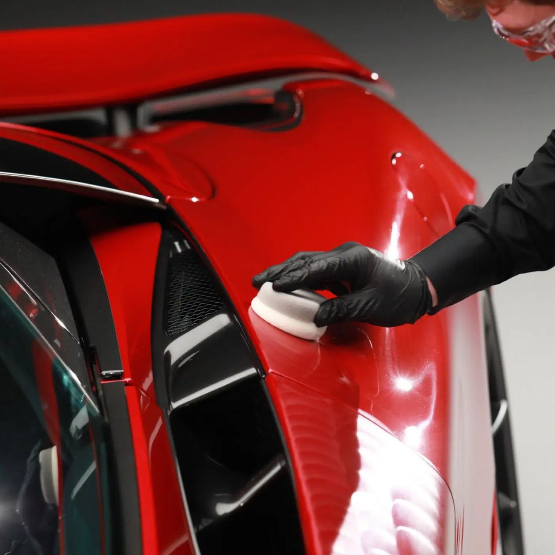 Person polishing a red car with a white polisher.