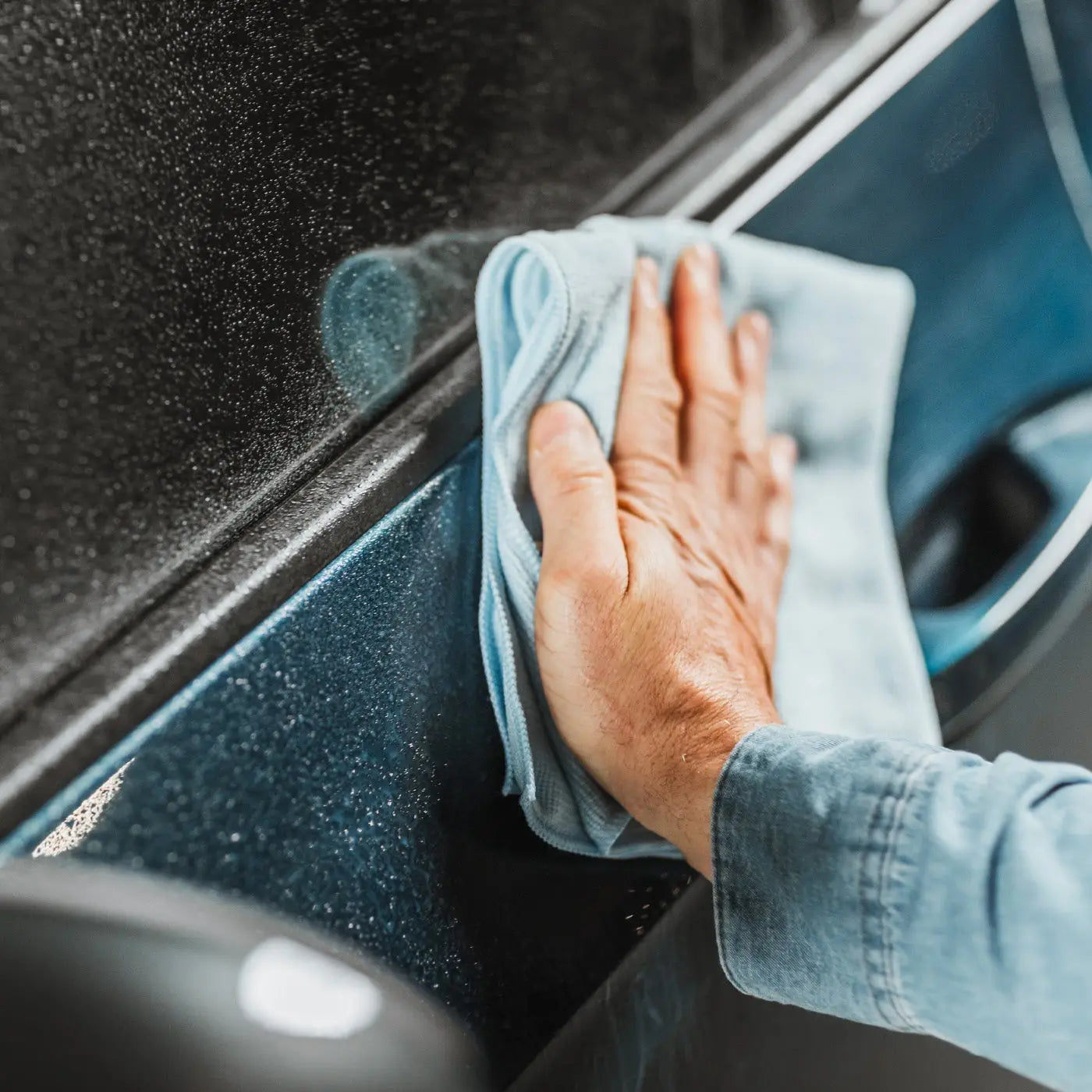 Hand cleaning a car window with a microfiber cloth