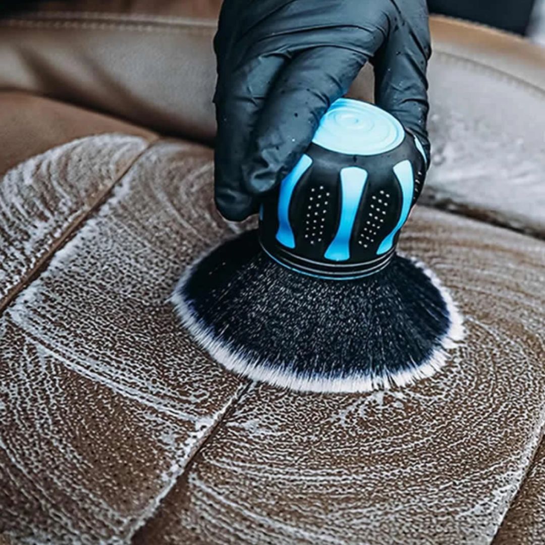 Cleaning brush with black bristles and blue accents being used on a leather surface.