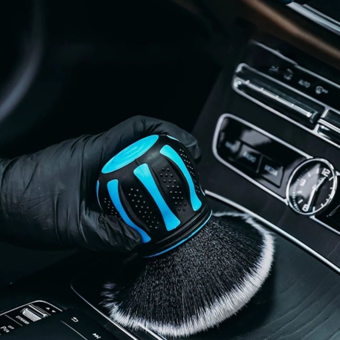 Car interior with a hand wearing a black glove holding a car detailing brush with blue accents.